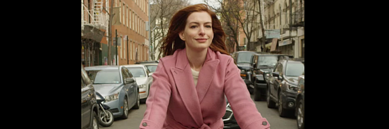 The First Time I Saw Myself On Screen as a Woman With Bipolar Disorder Anne Hathaway riding a bike through New York in a pink jacket