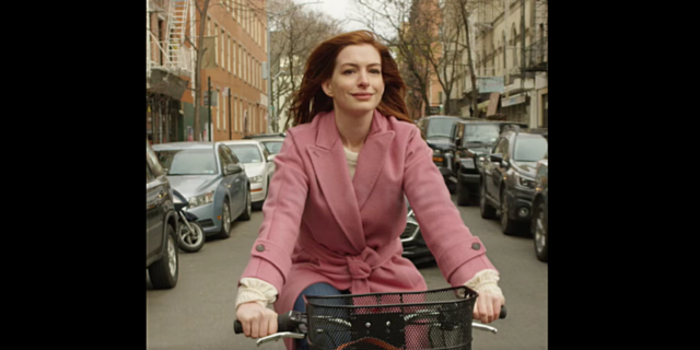 Anne Hathaway riding a bike through New York in a pink jacket