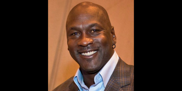 Michael Jordan, in a plaid brown suit, smiles at the camera