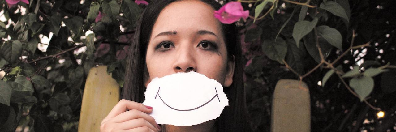 New Ken Burns Documentary Focuses on Youth Mental Health Young woman with long brown hair holding a hand-drawn smile on paper over her face