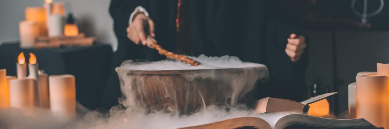 Person's hand holding a wand above a steaming cauldron