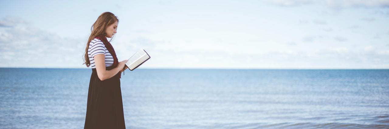 photo of woman standing on beach with bible