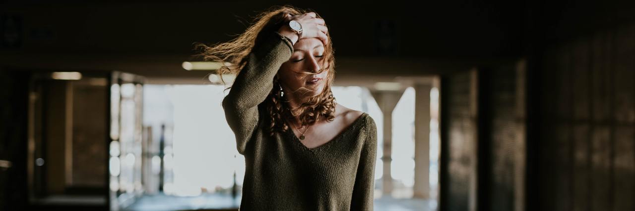Adult Children of Alcoholics May Feel Unusually Calm During COVID-19 woman in a green sweater walking through a garage with a hand in her hair