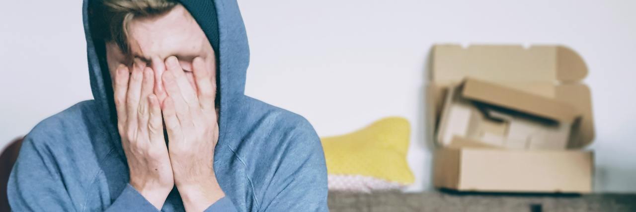 photo of man in hoodie sitting on sofa with his hands over his eyes, looking overwhelmed