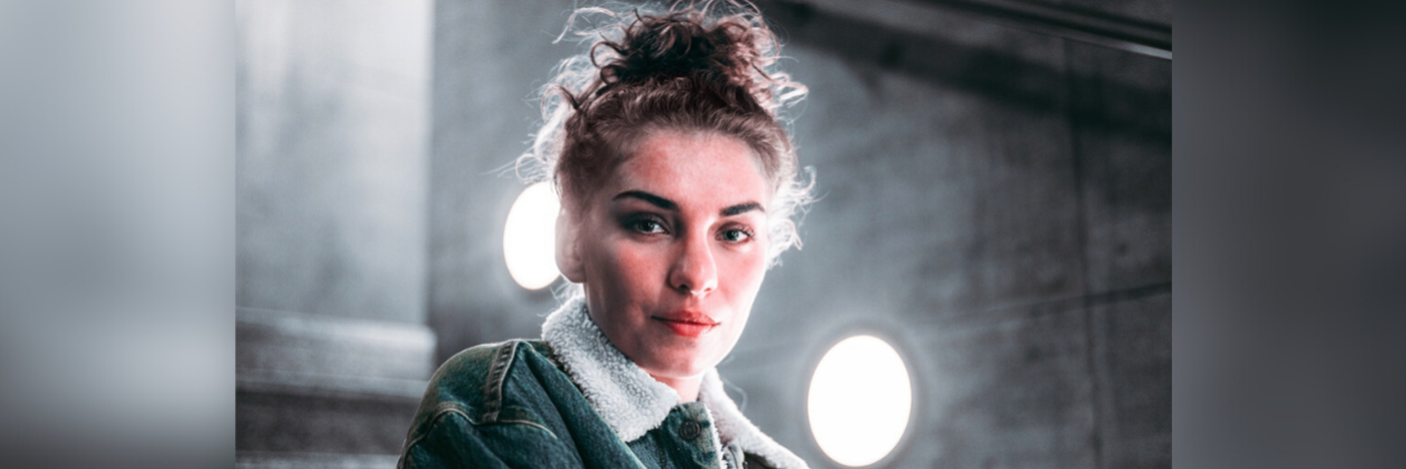 How Life During COVID-19 Is Like Living With Chronic Illness Woman looking at camera with lights behind her