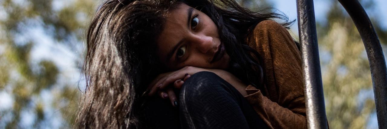 What People Don't See Underneath Borderline Personality Disorder photo of woman leaning on a seat outdoors, resting her head on her hands and looking into camera with sorrowful expression