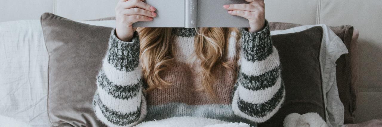 Why 'The Bell Jar' Is a Good Portrayal of Depression photo of woman sitting in bed reading a book which is covering her face