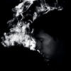 black and white photo of man in darkness with eyes closed and backlit smoke