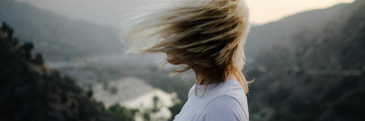 photo of woman with windblown blonde hair standing on clifftop