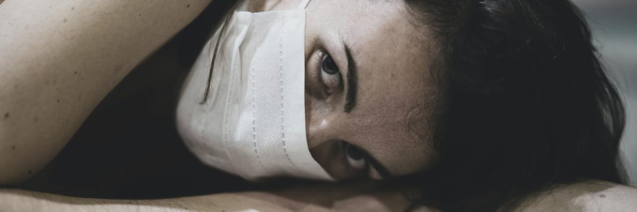 photo of woman lying on floor, wearing white face mask and looking into camera