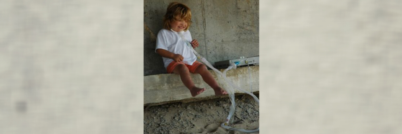 Our Young Son Lived His Life on a Ventilator young boy sitting outside with ventilator and smiling