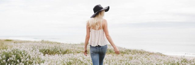 photo of woman walking through meadow or field with long white flowers