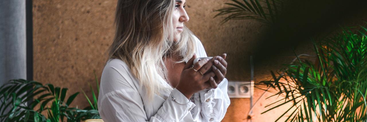 How to 'Hold Space' for Others During a Global Crisis Like COVID-19 photo of woman holding mug looking out of unseen window in soft light