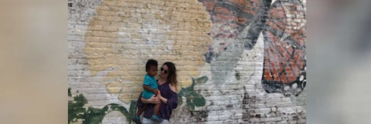 Living with Hashimoto’s: How I Navigate Thyroid Disease Woman holding toddler in front of mural on wall
