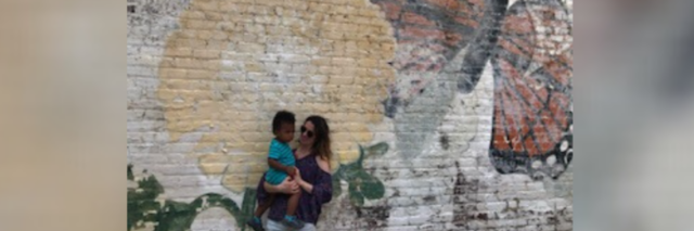 Woman holding toddler in front of mural on wall