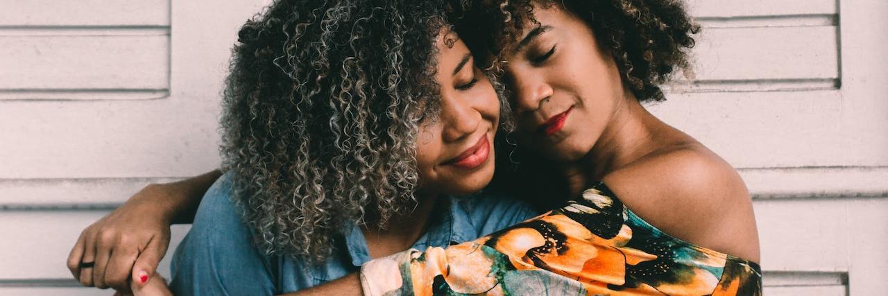 What Is Skin Hunger or Touch Starvation? Two black women with natural, curly hair, one with her arms around the other