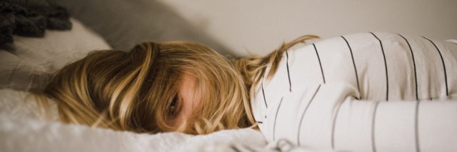 Blonde, white woman laying face down on a bed