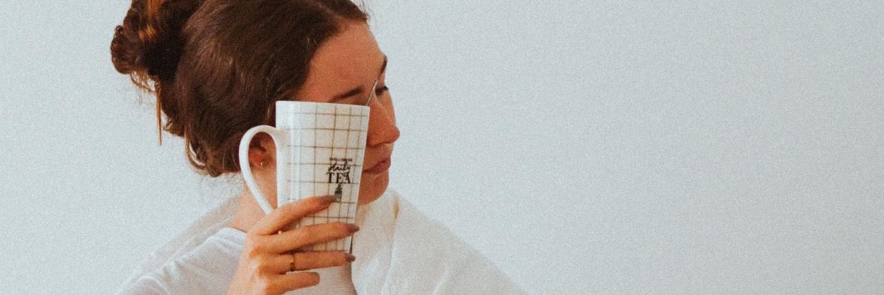 A woman in a blanket hiding her face behind a white mug