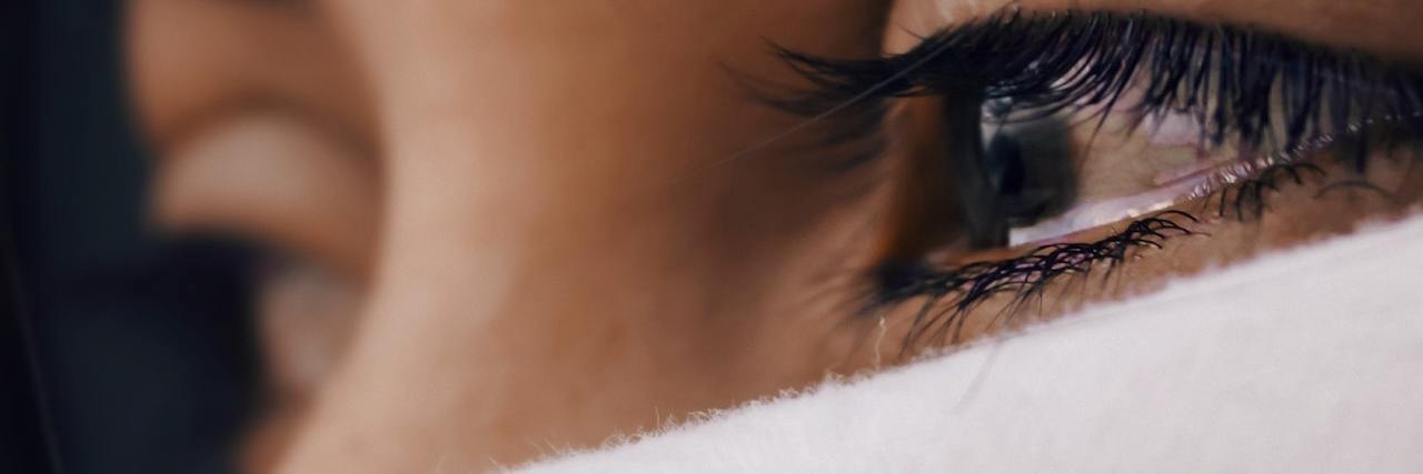 Close-up of a woman's face, which is partially covered by a white cloth, and you can see tears gathering in her eye