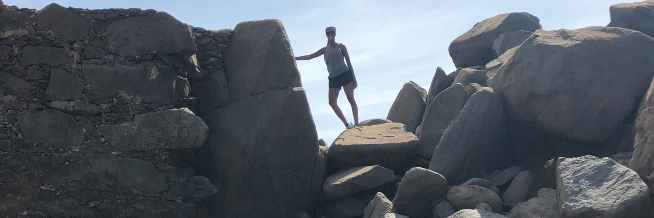 Why Seeking a Lupus Diagnosis Was Hard Despite Debilitating Symptoms Marthy standing on rocks with blue sky in the background.