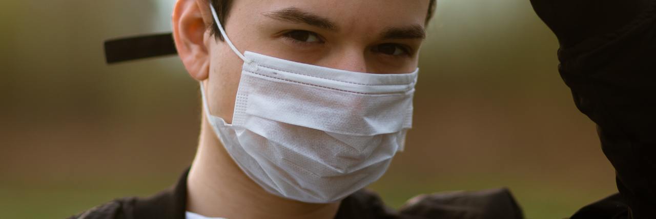 photo of young man wearing face mask and baseball cap, looking into