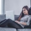 photo of woman lying on couch with laptop working from home