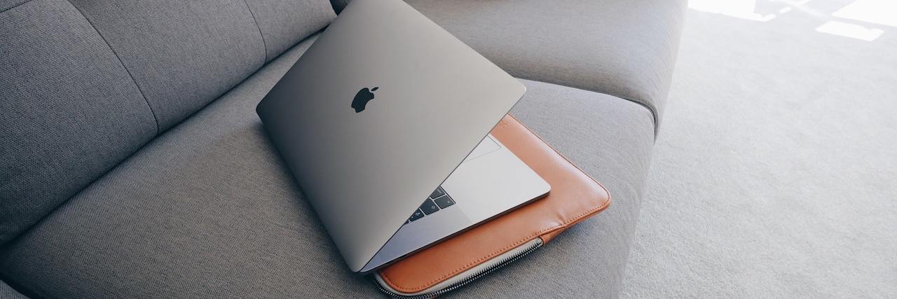 Mac laptop sitting on top of a leather computer case on a gray couch