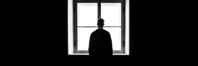 Man silhouetted against a window in black and white