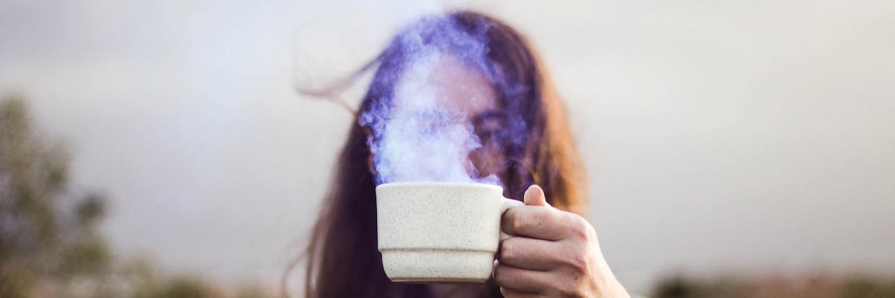 Woman holding steaming mug of coffee in front of her face