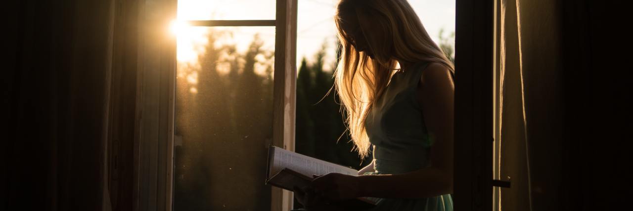 photo of woman sitting on table in golden sunlight, reading a book