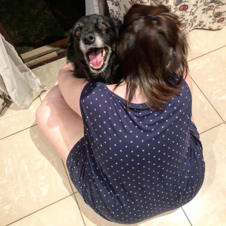 A woman cuddles with a black dog