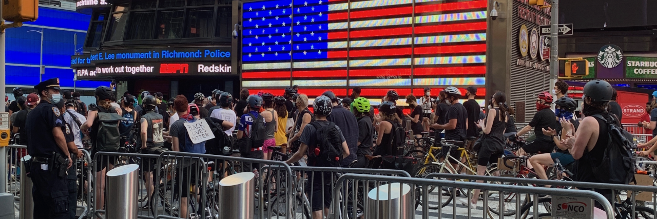 photo showing Black Lives Matter protest in Times Square, New York City, with protestors on bicycles in front of a sign showing the American flag
