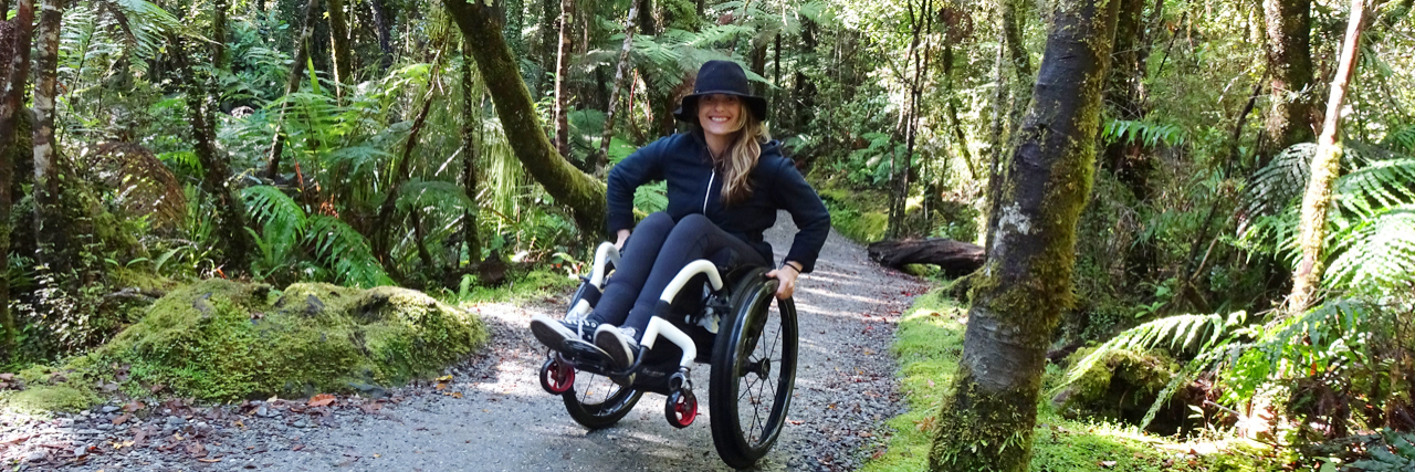 Advocating for Accessible Travel After a Spinal Cord Injury Ashley wheeling down a paved trail in the woods.