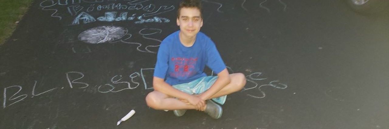 Birthday Lawn Bandit, a young white autistic boy sitting cross-legged on a driveway
