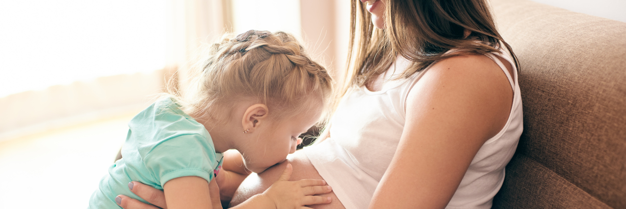 The Way Life Transitions After Becoming a Mom of Two a little girl is kissing her pregnant mother's belly