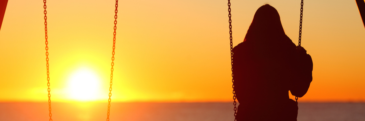 Solitary woman sitting on a swing looking at the sunset over the water