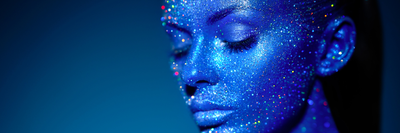 Woman with blue skin and sparkle rainbow glitter.