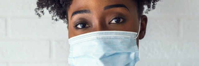 Portrait of young African-American woman wearing disposable medical face mask