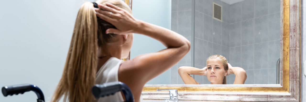 The Disability Community Needs to Talk About Our Internalized Ableism Girl in wheelchair looking in mirror.