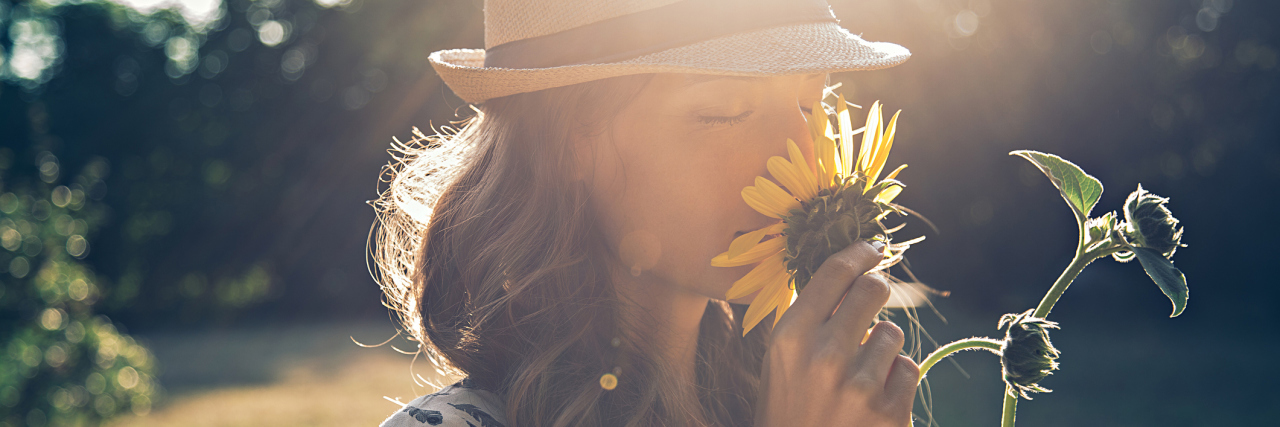 How I Learned to Love Myself as a Woman With Chronic Illness Woman smelling sunflower.