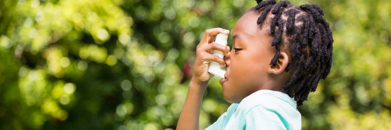 Black boy using an asthma inhaler in the park