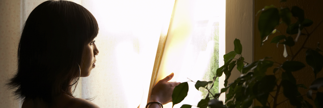 Have I Become Too Afraid of COVID-19? Woman pulling back curtains to look at the window.