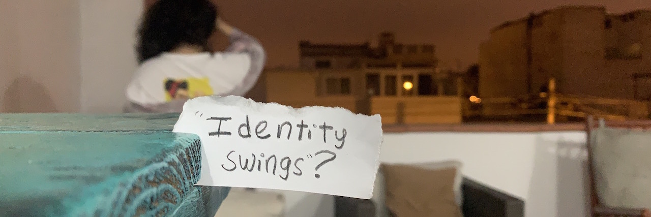 Borderline Personality Disorder: What Are Identity Swings? A woman's bedroom. She sits, unfocused on the background. In the front, a piece of paper says Identity Swings?