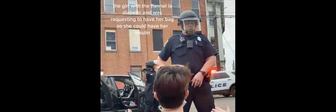 BLM Protests: Video Shows Girl With Diabetes Begging Cops to Get Bag screenshot from a video. Two sisters kneeling down in front of a cop