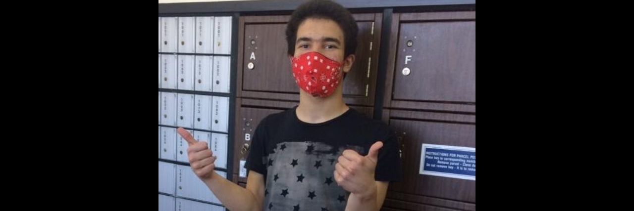 A teenage boy with autism wearing a mask and giving a thumbs up at the post office