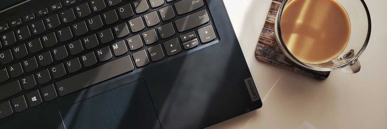 Legit Remote Jobs for People With a Disability or Chronic Illness Open laptop keyboard on the left with a cup of coffee on the right and a pen in front on a desk