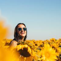photo of woman wearing sunglasses and smiling in a field of sunflowers