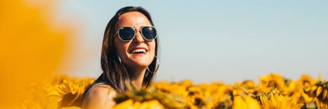 photo of woman wearing sunglasses and smiling in a field of sunflowers