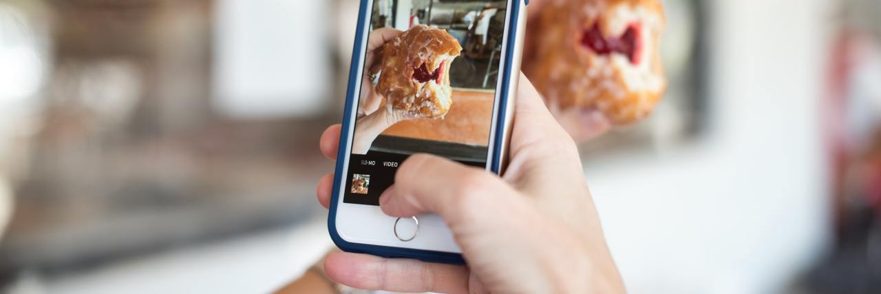 photo of person's hands holding phone and taking an Instagram photo of a donut