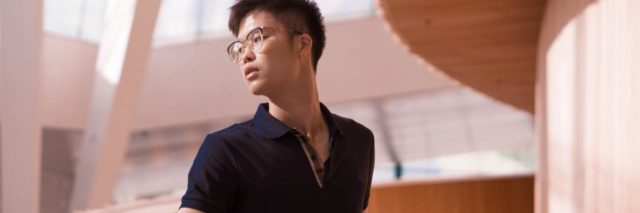 photo of asian man looking over his shoulder while leaning on a wooden balcony
